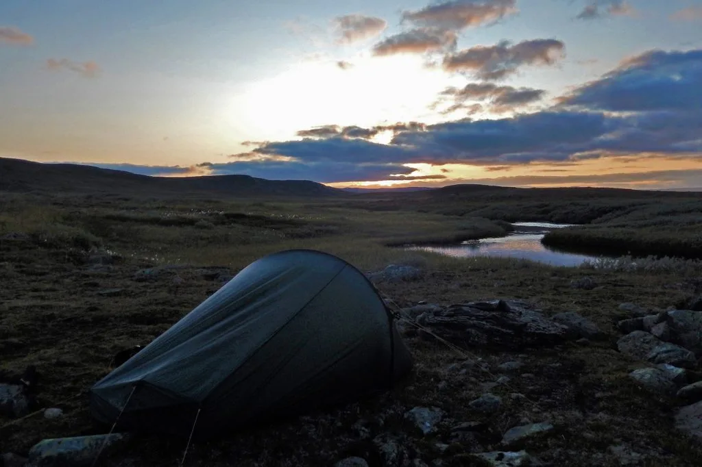 Telt i solnedgang ved en elv.